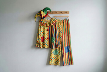 Colorful clown costume hanging on a plain white wall, minimalist concept. © JOE