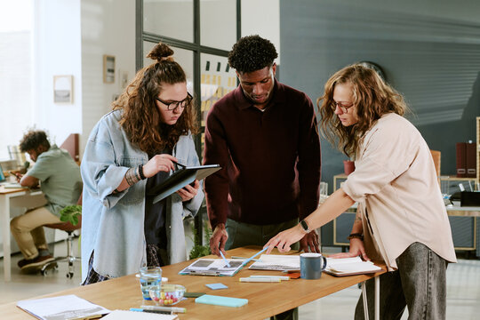 Young adult Caucasian woman, young adult Black man, and young adult Caucasian woman collaborating on project, reviewing documents and discussing ideas at modern office table - Powered by Adobe