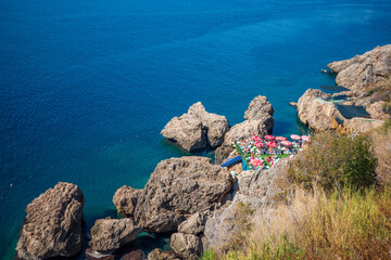 A stunning Mediterranean seaside scene featuring large rocky formations, crystal-clear turquoise...