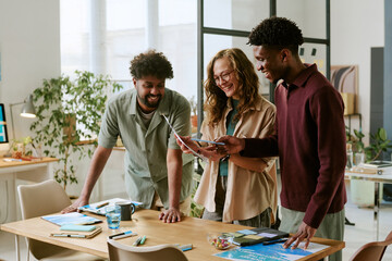 Multiethnic group of young adults collaborating around desk, reviewing documents and discussing project ideas in modern office setting, smiling and engaging with each other