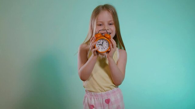 Funny girl in a T-shirt and shorts sets the time on the alarm clock. The child holds the clock in her hands and smiles.