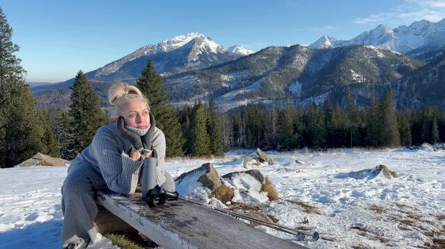 Woman sitting with walking sticks on snowy mountains background
