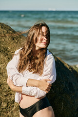 Young woman with long hair embraces herself near Baltic Sea shore