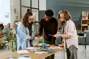 Group of young adult multiethnic colleagues collaborating around table, discussing documents and...