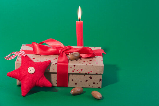 Christmas gift box with red burning candle and red star and beechnuts on green background