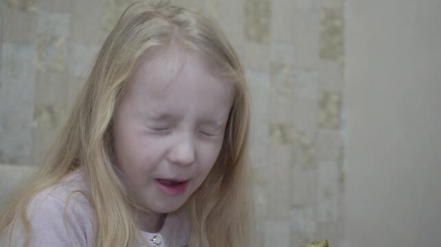 Little girl eating cucumber winces from sour taste, Little girl with white hair eats cucumber winces from sour taste