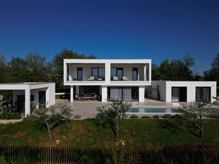 Modern luxury villa with pool, terraces, and clean minimalist architecture captured by drone. Bright sunny day, surrounding greenery, and contemporary outdoor living areas