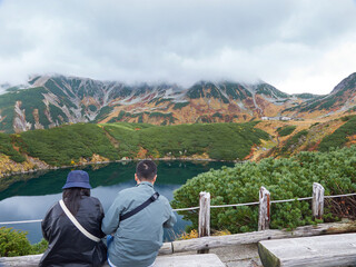 Naklejka premium 秋の観光名所立山黒部アルペンルートの室堂山頂のみくりが池で休憩するシニア男女観光客の姿と山の風景