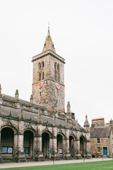 Obraz premium Old stone clock tower with arched walkway and courtyard, historic architecture under cloudy sky
