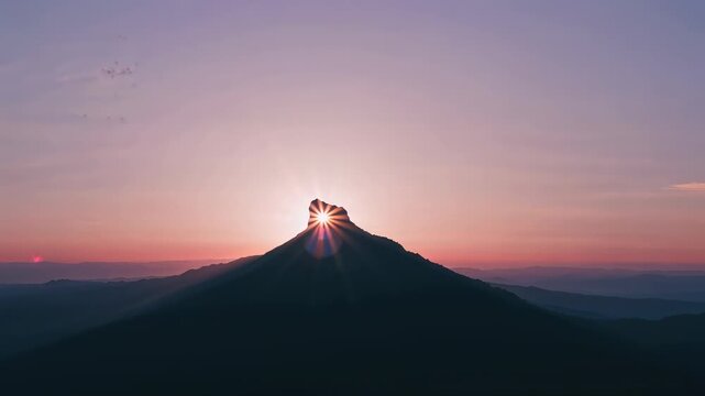 Rising sun aligning behind mountain notch at dawn, producing starburst, lens flare, and beams