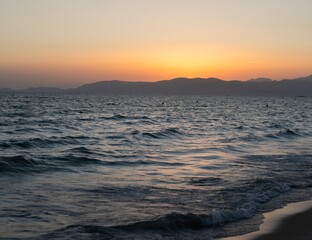 Sunset over the Mediterranean Sea with Silhouettes of Swimmers and Mountains
