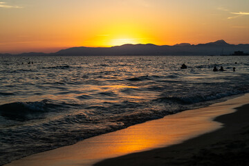 Sunset over the Mediterranean Sea with Silhouettes of Swimmers and Mountains