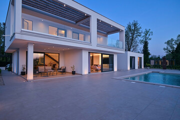 Exterior view of a modern luxury house with a swimming pool at twilight. Illuminated two-story...