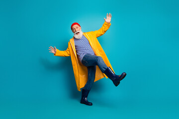 Obraz premium Joyful bearded man in yellow raincoat kicks playfully against blue background