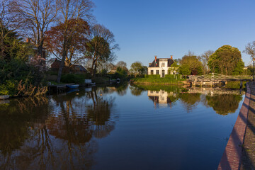 Quiet scene with a white house, drawbridge, and perfect reflections in the canal water in Bedum, Groningen. Soft morning sunlight