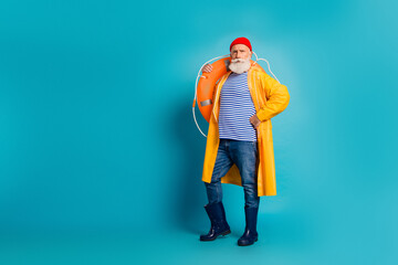 Bearded man in a bright yellow raincoat with lifebuoy poses against a blue studio backdrop