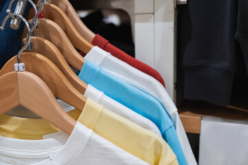 Row of colorful cotton t-shirts on wooden hangers with size tags organized on a rack in a fashion...