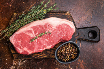 Raw New York strip beef steak, also named Striploin steak on a wooden board. brown background. top view