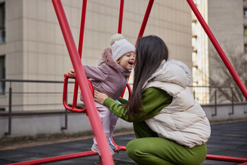 Mother pushing happy daughter on a swing set in an urban playground