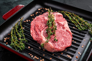 Raw Rib eye steak in a grill skillet with herbs, prime beef meat. black background. top view