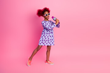 Young girl sings into a microphone in a playful pink studio wearing a purple polka dot dress and sneakers