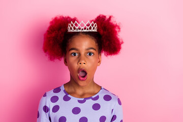Young girl with tiara stands against pink background wearing purple polka dot shirt with surprised expression © deagreez