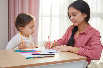 Mother and cute little daughter drawing with colored pencils, engaging in creative home learning
