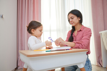 Mother and daughter cutting designs from paper with scissors for an art project