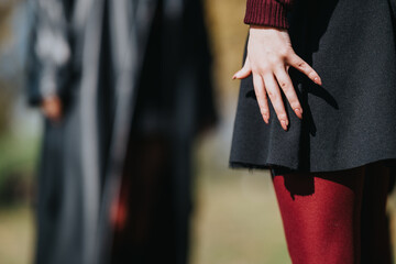 Fototapeta premium A close-up of a stylish woman outdoors, wearing a dark coat and bold red tights, with a graceful hand pose. The scene conveys fashion, mood, and urban sophistication in natural light.