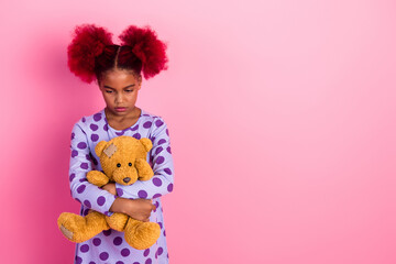 Young girl with pink hair stands with a teddy bear against a pink background