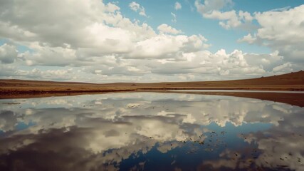 Cumulus clouds drifting under gentle breeze over plain pond, creating shifting water reflections - Powered by Adobe
