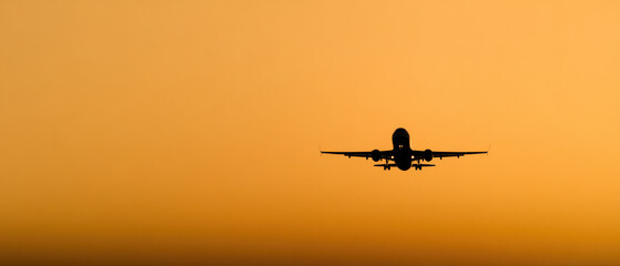 Front view of a commercial airplane in silhouette as it ascends into a vibrant orange sky during sunset, symbolizing travel and freedom.  
 