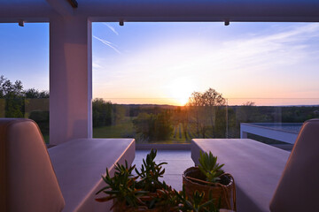 Fototapeta premium Sunset view from a luxurious modern patio with lounge chairs, overlooking a tranquil green landscape of trees and vineyards, perfect for a relaxing evening