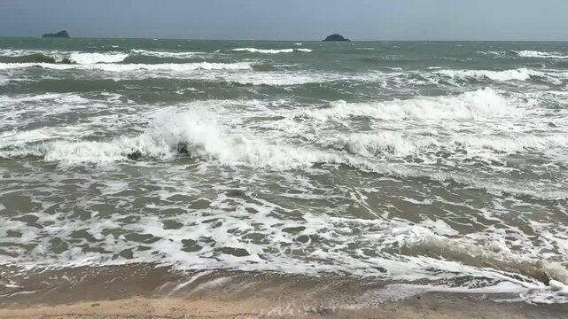 video of windy ocean waves pushing foamy water onto sandy beach with active coastal motion
