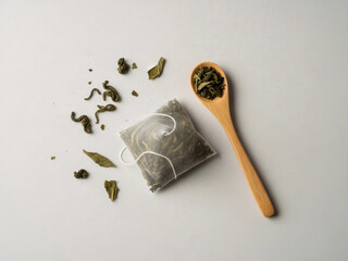 Minimal composition with green tea bag, loose leaf tea and wooden spoon on clean white background