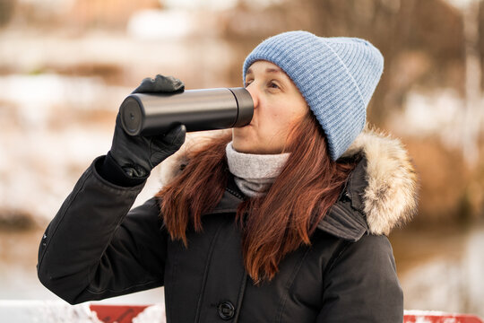 Thermos in winter. Woman and hot coffee from thermo bottle in nature. Drinking tea from thermal flask. Warm beverage from mug on cold day outdoors.