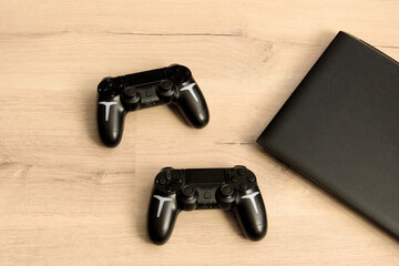 Two game controllers and laptop on a wooden desk. Technology, gaming, break from work. © Yanina