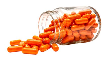 Health supplement: bright orange capsules scattered from a spilled glass bottle