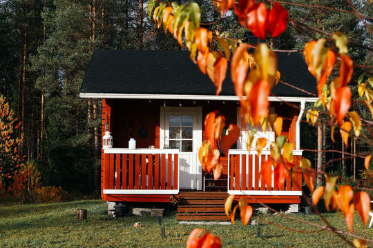 Cozy wooden cabin surrounded by vibrant autumn foliage, featuring a welcoming porch and lush green grass, creating a serene and picturesque rural atmosphere