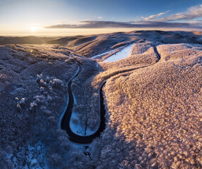 An aerial drone view of a snow - covered forest on a hill in the sunrise in Slovakia