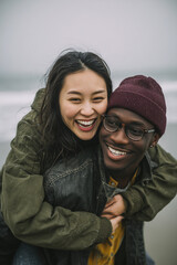 An attractive young black man wearing glasses and a maroon beanie, giving a piggyback ride to his Asian girlfriend with dark hair.