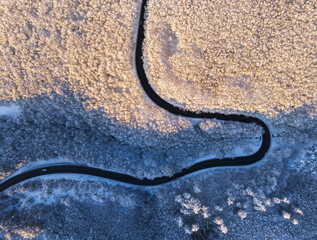 Aerial view of winter landscape with snow covered mountain hills and winding forest road in morning