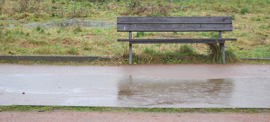 An old wooden park bench near a dirt path during the rain