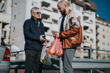 Two men, an elderly man and a younger shopper, share a moment while exchanging grocery bags on a sunny city street. A casual, friendly urban interaction between generations.