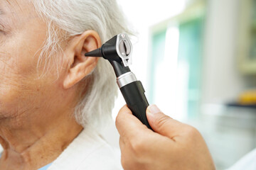 Otolaryngologist or ENT physician doctor examining senior patient ear with otoscope, hearing loss problem.