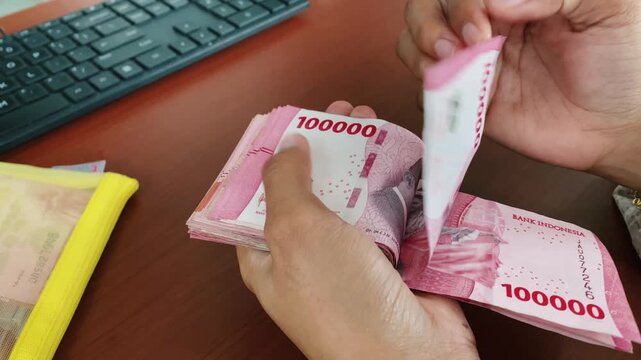 Careful cash counting process using indonesian rupiah notes.