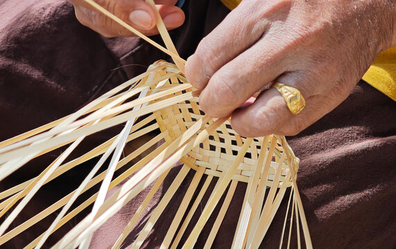 The hands are weaving a bamboo basket.