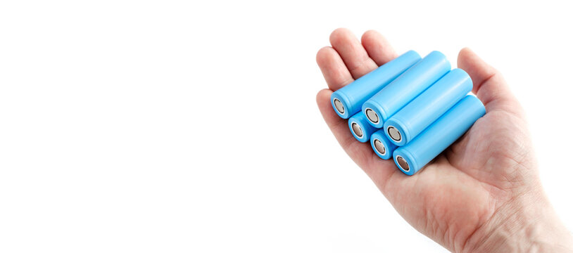 Hand holds light blue rechargeable lithium-ion battery type 18650 for electrical appliances and devices, on isolated background, with space for text.