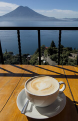 coffee cup on table with scenic view lake atitlan antigua guatemala blue water sunny volcano crater pond outdoor travel tourism adventure getaway cappuccino late milk cafe restaurant flavor santa cruz