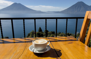 coffee cup on table with scenic view lake atitlan antigua guatemala blue water sunny volcano crater pond outdoor travel tourism adventure getaway cappuccino late milk cafe restaurant flavor santa cruz